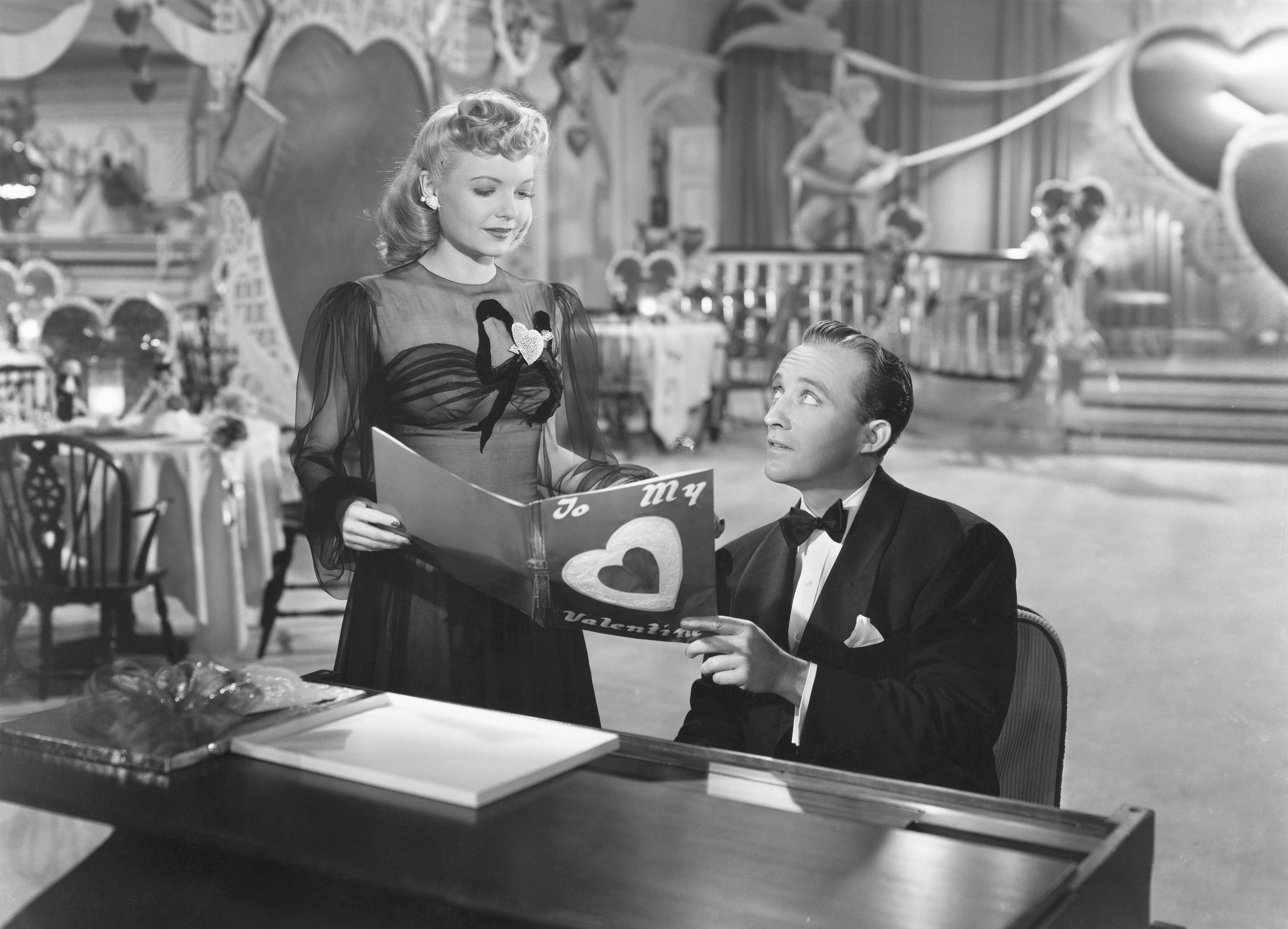 Marjorie Reynolds joins Bing Crosby at the piano to look at a Valentine in the 1942 musical <em>Holiday Inn.</em>